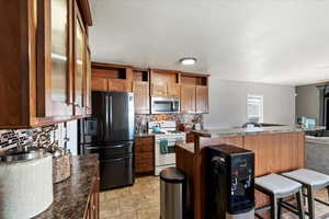 Kitchen featuring stainless steel appliances, light tile patterned floors, a kitchen breakfast bar, and decorative backsplash