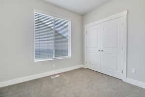 Bedroom with multiple windows, light colored carpet, and a closet