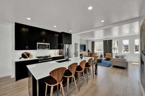 Kitchen with sink, a kitchen island with sink, a kitchen bar, appliances with stainless steel finishes, and light hardwood / wood-style floors