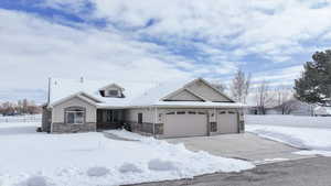 View of front of house with stone siding, driveway, an attached garage, and fence