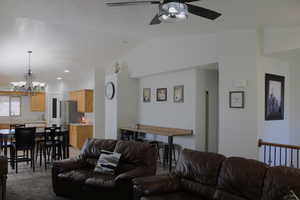 Living room with sink, vaulted ceiling, light colored carpet, and ceiling fan with notable chandelier