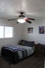 Carpeted bedroom featuring a textured ceiling and ceiling fan