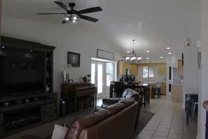 Living room with lofted ceiling, light tile patterned flooring, and ceiling fan with notable chandelier