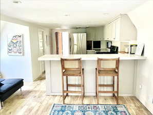 Kitchen featuring light wood-type flooring, a kitchen bar, stainless steel fridge, and kitchen peninsula