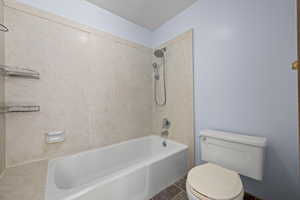 Bathroom with tile patterned floors, tiled shower / bath, and toilet