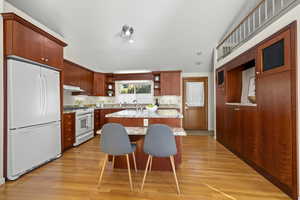 Kitchen with a kitchen breakfast bar, vaulted ceiling, white appliances, light wood-type flooring, and sink