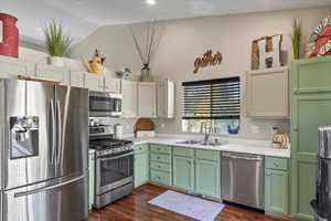 Kitchen featuring dark wood-type flooring, sink, lofted ceiling, white cabinetry, and appliances with stainless steel finishes