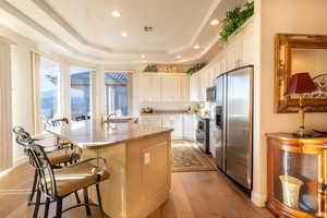 Kitchen with light stone counters, white cabinetry, light hardwood / wood-style flooring, stainless steel appliances, and a center island with sink