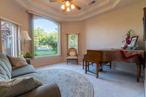 Sitting room with ceiling fan, light colored carpet, and a raised ceiling