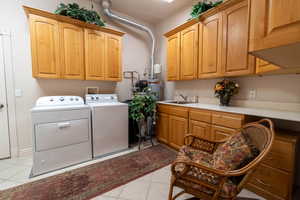 Laundry area featuring light tile patterned flooring, sink, cabinets, water heater, and washer and dryer