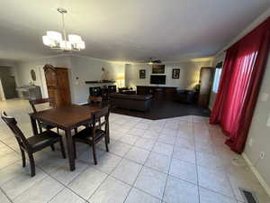 Tiled dining space with ceiling fan with notable chandelier and ornamental molding