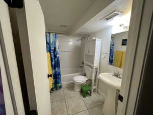 Bathroom with a textured ceiling, shower / tub combo, toilet, and tile patterned floors