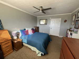 Bedroom with carpet floors, a textured ceiling, ornamental molding, and ceiling fan