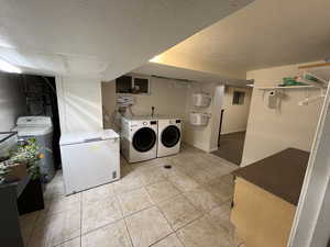 Laundry area with a textured ceiling, washing machine and dryer, and light tile patterned floors