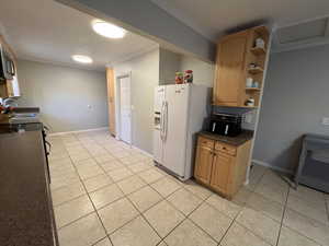 Kitchen with white fridge with ice dispenser, light tile patterned floors, sink, and ornamental molding