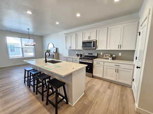 Kitchen with appliances with stainless steel finishes, white cabinetry, sink, and a center island with sink