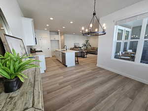 Kitchen with light hardwood / wood-style flooring, hanging light fixtures, a center island with sink, sink, and white cabinetry