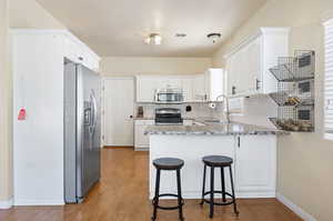 Kitchen with appliances with stainless steel finishes, sink, kitchen peninsula, and white cabinetry