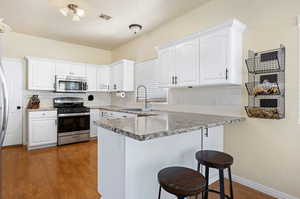 Kitchen with appliances with stainless steel finishes, sink, dark wood-type flooring, and white cabinets