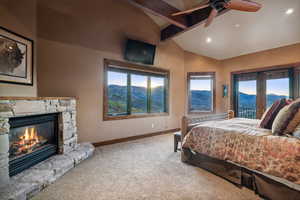 Bedroom with vaulted ceiling with beams, multiple windows, ceiling fan, and a stone fireplace