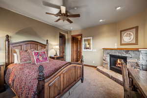 Carpeted bedroom with ceiling fan and a stone fireplace