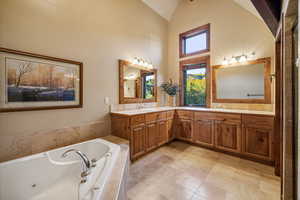 Bathroom with vanity, high vaulted ceiling, and a relaxing tiled tub