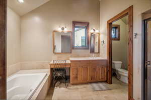 Bathroom featuring lofted ceiling, tiled bath, vanity, and toilet