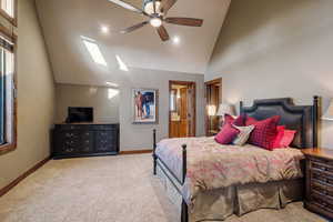 Carpeted bedroom featuring high vaulted ceiling, ceiling fan, and a skylight