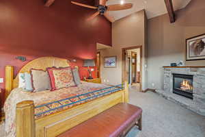 Carpeted bedroom featuring high vaulted ceiling, ceiling fan, beamed ceiling, and a stone fireplace