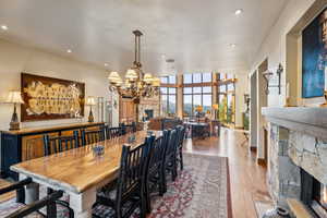 Dining area with an inviting chandelier, a stone fireplace, a wall of windows, and light wood-type flooring