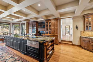 Kitchen featuring light hardwood / wood-style floors, sink, an island with sink, a stone fireplace, and dark stone countertops