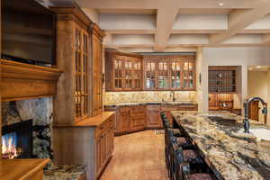 Bar with light hardwood / wood-style floors, coffered ceiling, tasteful backsplash, dark stone counters, and sink