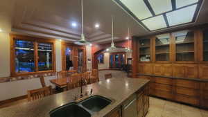 Kitchen featuring a tray ceiling, dishwasher, sink, decorative light fixtures, and dark stone countertops