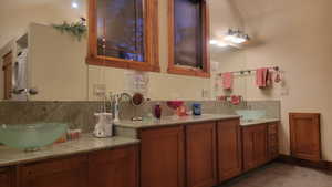 Bathroom featuring vanity, vaulted ceiling, and tasteful backsplash