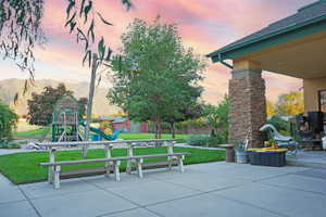 Patio terrace at dusk with a playground, a mountain view, and a yard