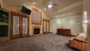 Interior space featuring rail lighting, a tiled fireplace, lofted ceiling, ceiling fan, and carpet