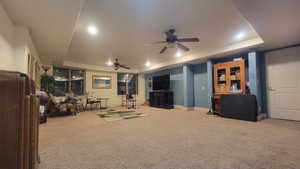 Living room with ceiling fan, carpet floors, and a raised ceiling