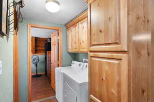 Clothes washing area with a textured ceiling, hardwood / wood-style flooring, independent washer and dryer, and cabinets