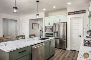 Kitchen with pendant lighting, an island with sink, tasteful backsplash, stainless steel appliances, and dark hardwood / wood-style flooring