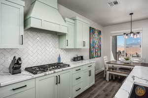 Kitchen featuring stainless steel gas cooktop, an inviting chandelier, premium range hood, dark hardwood / wood-style floors, and green cabinets