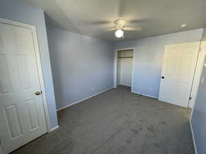 Unfurnished bedroom with dark carpet and ceiling fan