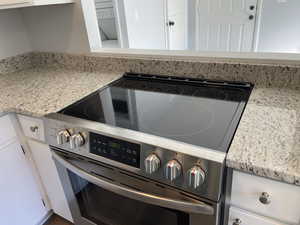 Interior details featuring light stone counters, washer / clothes dryer, white cabinetry, and stainless steel electric range