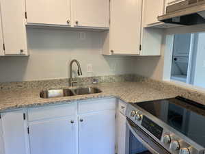 Kitchen featuring white cabinets, sink, stainless steel electric range, light stone countertops, and stacked washer / drying machine