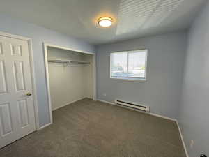 Unfurnished bedroom with a baseboard radiator, carpet, a closet, and a textured ceiling