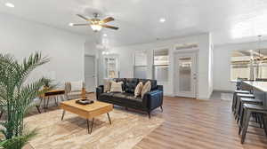 Living room featuring light wood-type flooring, ceiling fan with notable chandelier, and a textured ceiling