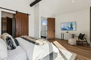 Bedroom with a barn door, dark wood-type flooring, and high vaulted ceiling