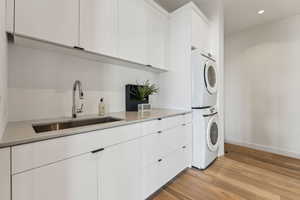 Washroom with cabinets, stacked washer and clothes dryer, sink, and light hardwood / wood-style floors