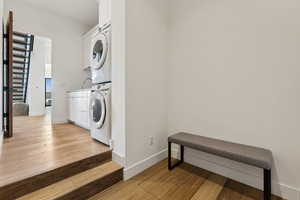 Washroom with stacked washer / drying machine and light wood-type flooring