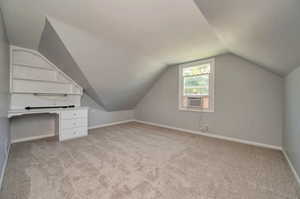 Additional living space with cooling unit, light colored carpet, and vaulted ceiling