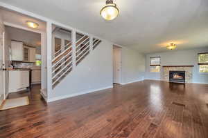 Unfurnished living room with a stone fireplace and dark hardwood / wood-style floors